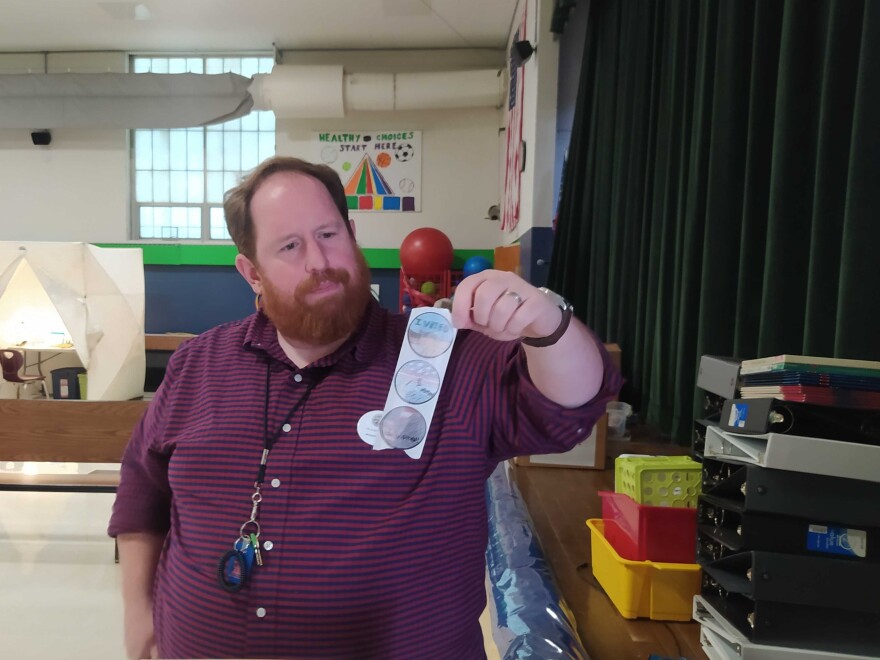 Ward 11 Moderator Michael Wolf shows off the new "I Voted" stickers drawn by local 4th graders at the school gym of Gossler School on Primary Day; Tuesday, Sept. 10, 2024.