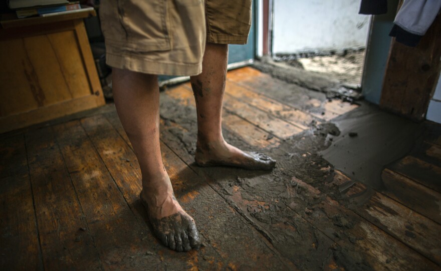 The bare, muddy feet of a person wearing shorts and standing on a wood floor