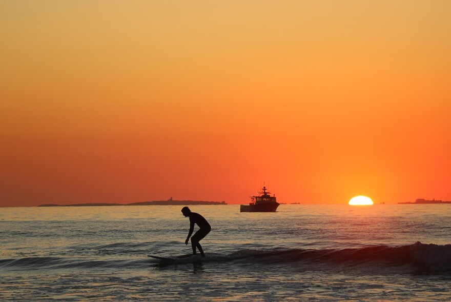 A surfer and fishing vessel make the most of a September morning at sunrise in Rye, New Hampshire. Dan Tuohy photo 2019.