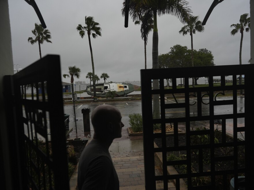 Christian Burke stands at the door of his home, where he, his mother, and his aunt plan to ride out Hurricane Milton on the third floor overlooking overlooking Tampa Bay, in Gulfport, Fla., Wednesday, Oct. 9, 2024. Burke, who said his engineer father built the concrete home to withstand a Category 5 hurricane, expects his raised ground floor to get up to 8 feet of water in Milton. A boat deposited by Hurricane Helene sits lodged in the bay front park outside his front door.