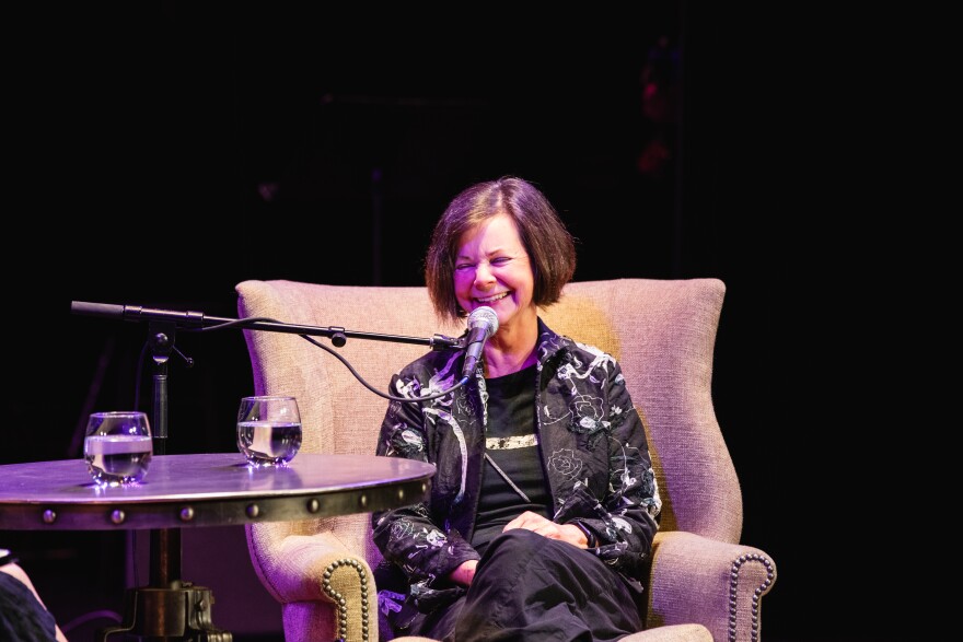  Geraldine Brooks, a dark-haired woman, sits in an armchair in front of a microphone