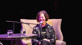  Geraldine Brooks, a dark-haired woman, sits in an armchair in front of a microphone