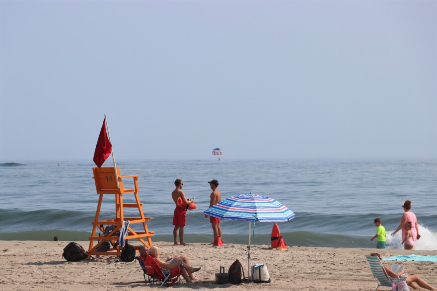  Two lifeguards stand on Hampton Beach on a bright day. A person is parasailing over the ocean in the horizon. 