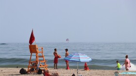  Two lifeguards stand on Hampton Beach on a bright day. A person is parasailing over the ocean in the horizon. 