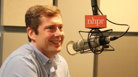 A man wearing a blue button up shirt smiles into a radio microphone