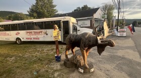 A wooden moose sculpture in front of a ;arge tour bus