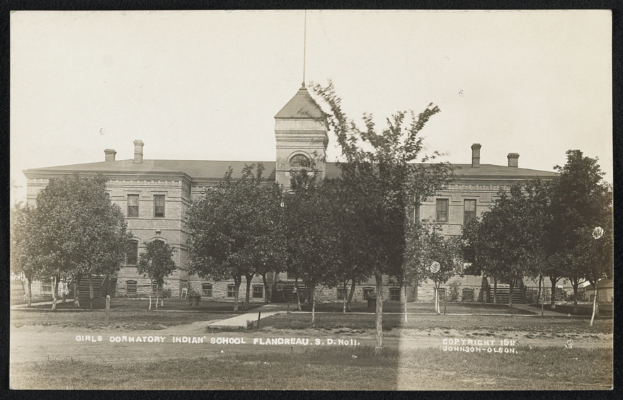 A black and white postcard showing a large building with trees in front of it reading "girls dormatory indian school flandreau S.S. No 11."