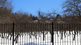 White spires of Green Mountain Treatment Center are seen behind a tall black fence and rows of leafless trees in snow.