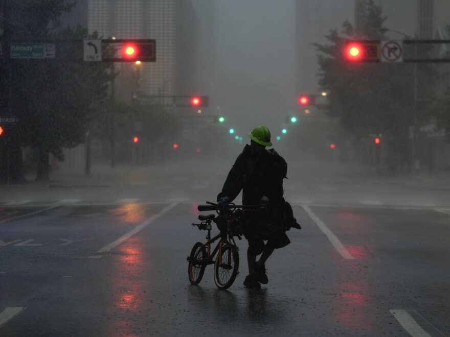 Ron Rook, who said he was looking for people in need of help or debris to clear, walks through windy and rainy conditions on a deserted street in downtown Tampa, Fla.,