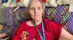 A portrait of Lorraine Blanchard, seated on a couch and wearing a red shirt and necklace with a cross.