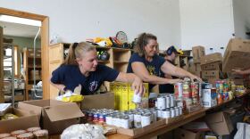 Two people lean over a table, arranging cans of food.