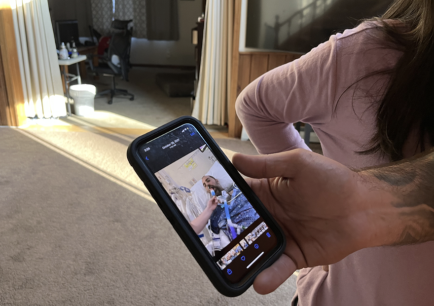 Mark McEnnis's hand holds his phone, and on the screen is a photo of him while he was hospitalized for COVID.