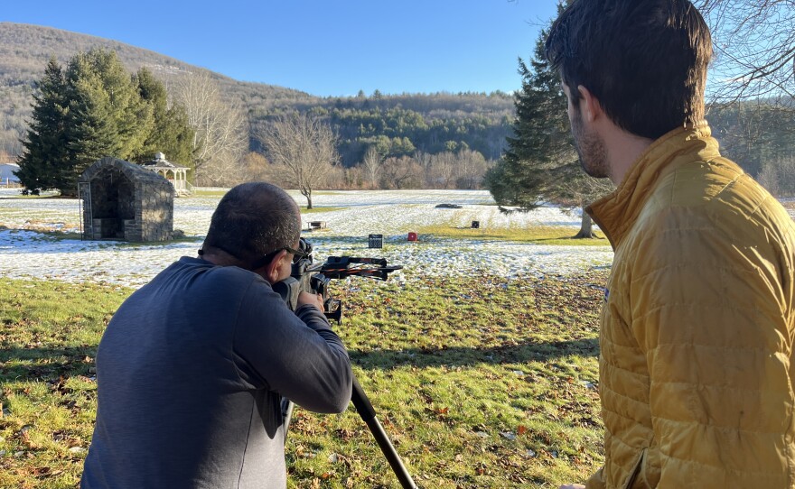 Tim instructs Jose how to shoot a crossbow.