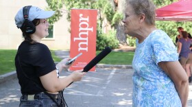 A young woman on the left has a recording kit and mic which she holds up for an older woman on the right to speak into. They are both smiling. 