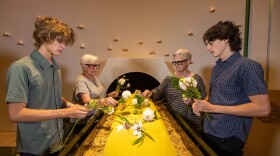 Guests demonstrate placing flowers on a shrouded mannequin in Recompose's Gathering Space. Decedents here are surrounded by wood chips and alfalfa, and placed in a special vessel that encourages decomposition.