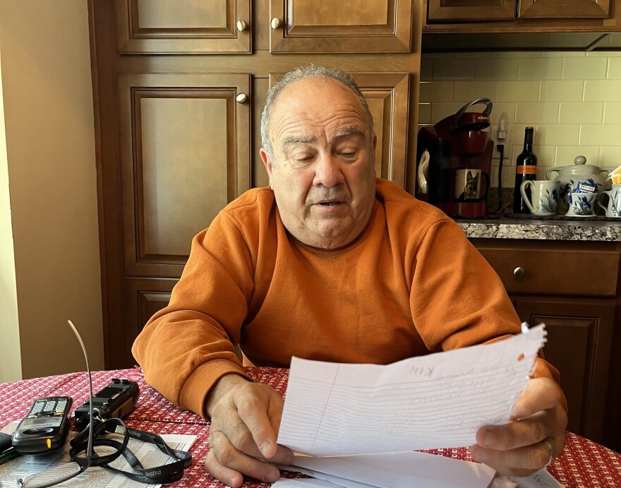 A man sitting at a kitchen table holds up a piece of notebook paper