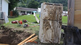 A muddy fridge sits outside of a building