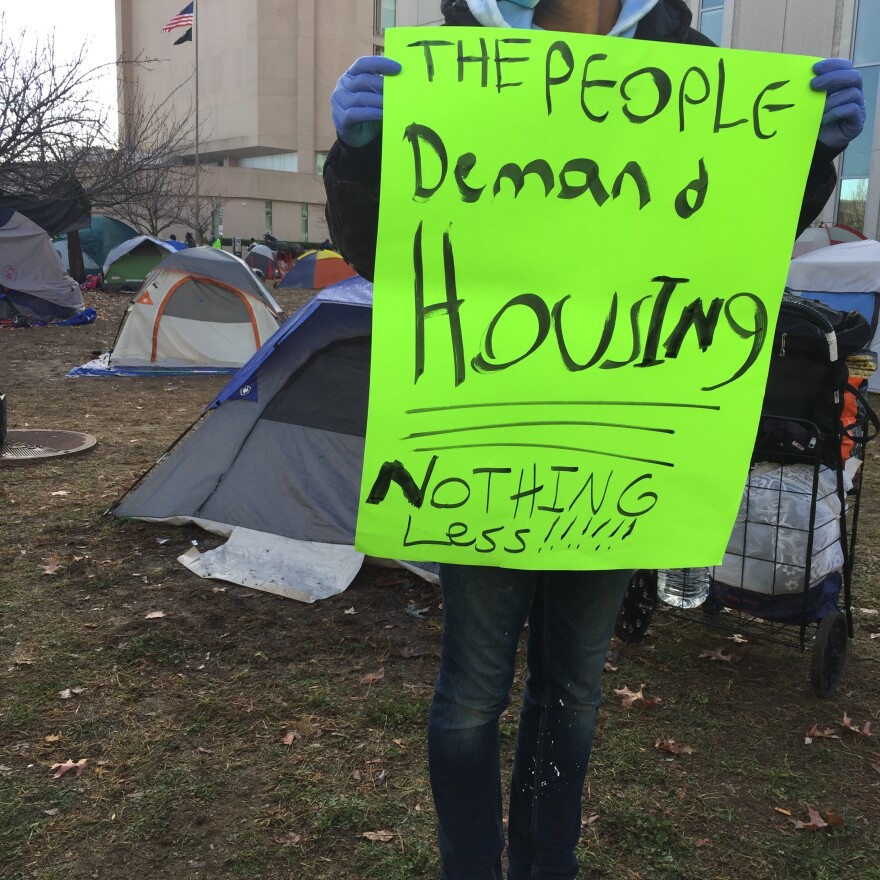 Photo of man holding sign that says the people demand housing