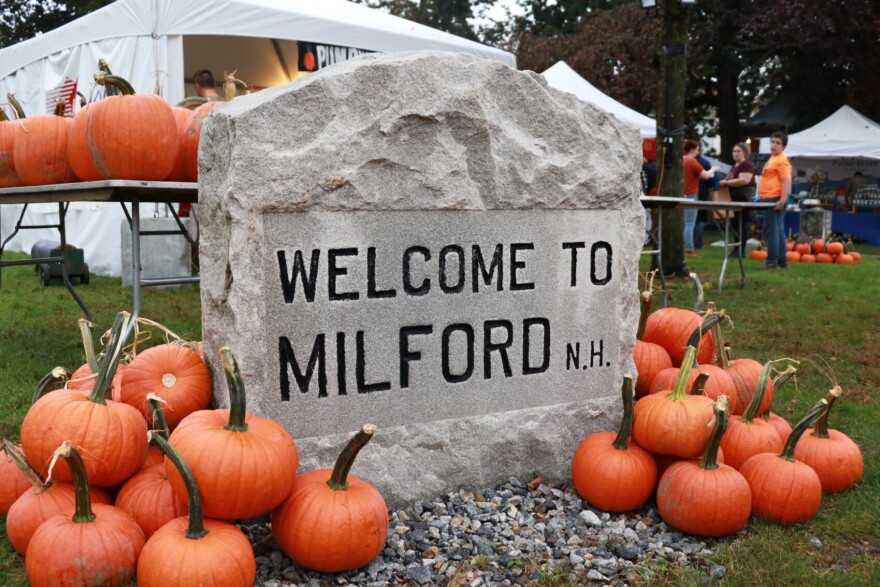 A stone sign that reads "Welcome to Milford, N.H." surrounded by pumpkins at the 2023 Milford Pumpkin Festival