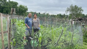 Two people stand together in a garden plot looking at the camera