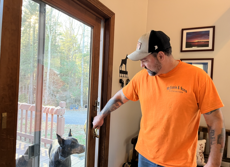 Mark McEnnis stands inside his home, while his dog looks from outside a sliding glass door.