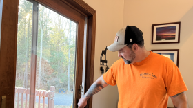 Mark McEnnis stands inside his home, while his dog looks from outside a sliding glass door.