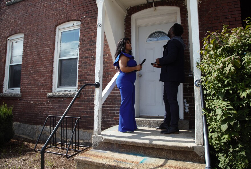 A woman in a blue jumpsuit and a man wearing a black jacket stand in front of an apartment building door in their efforts to get the word out about the state's rental assistance program. 