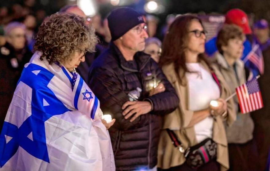 Elise White of Nashua holds a candle as she wraps herself in the Israeli flag during the vigil at the State House on Monday evening, October 7, 2024, to commemorate the first anniversary of the Hamas attack on Israel. GEOFF FORESTER / Monitor staff