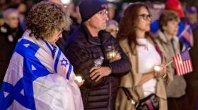 Elise White of Nashua holds a candle as she wraps herself in the Israeli flag during the vigil at the State House on Monday evening, October 7, 2024, to commemorate the first anniversary of the Hamas attack on Israel. GEOFF FORESTER / Monitor staff