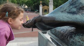 A child leans over to jokingly sniff a bronze statue of a foot, with an amused expression.